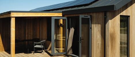 A wooden cabin with a deck, a sliding glass door, and a chair.
