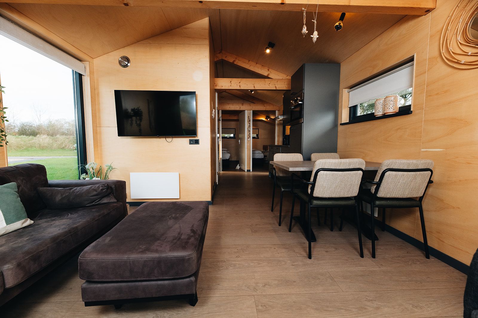 Ein modernes Interieur mit einer Couch, einem Hocker, einem Esstisch, Stühlen und einem Wand-Fernseher.
