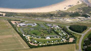 An aerial view of a coastal resort with a beach, caravan park, and surrounding greenery.