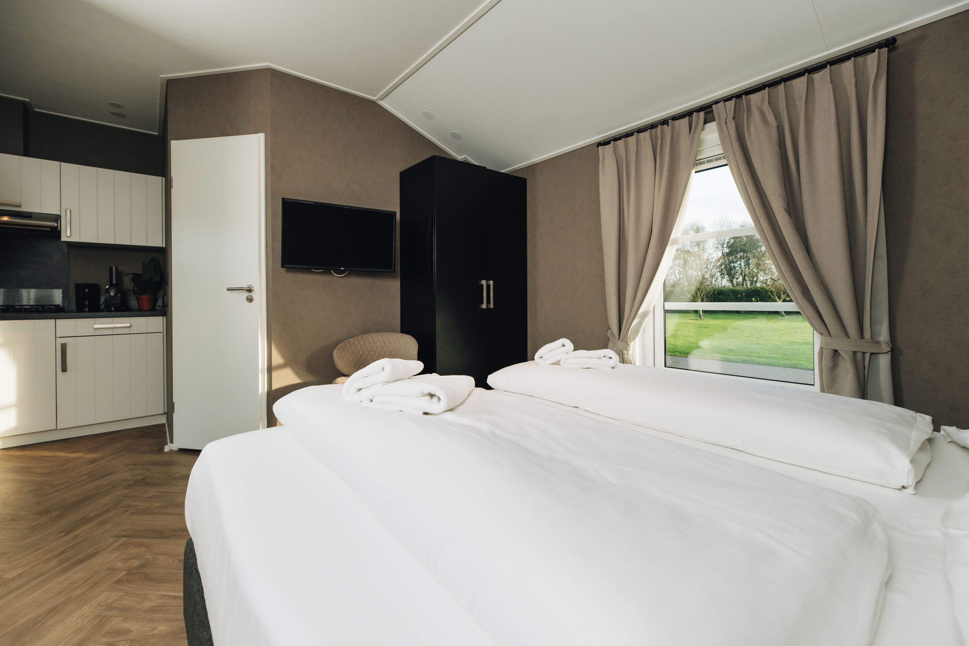 Quarto de hotel com cama, televisão, guarda-roupa e vista para o exterior.