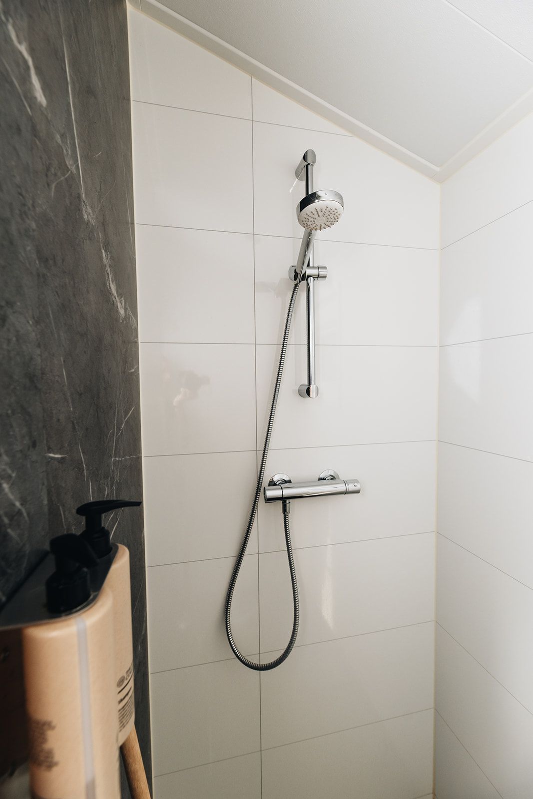 A shower with a handheld showerhead and a handheld hose, mounted on a tiled wall.