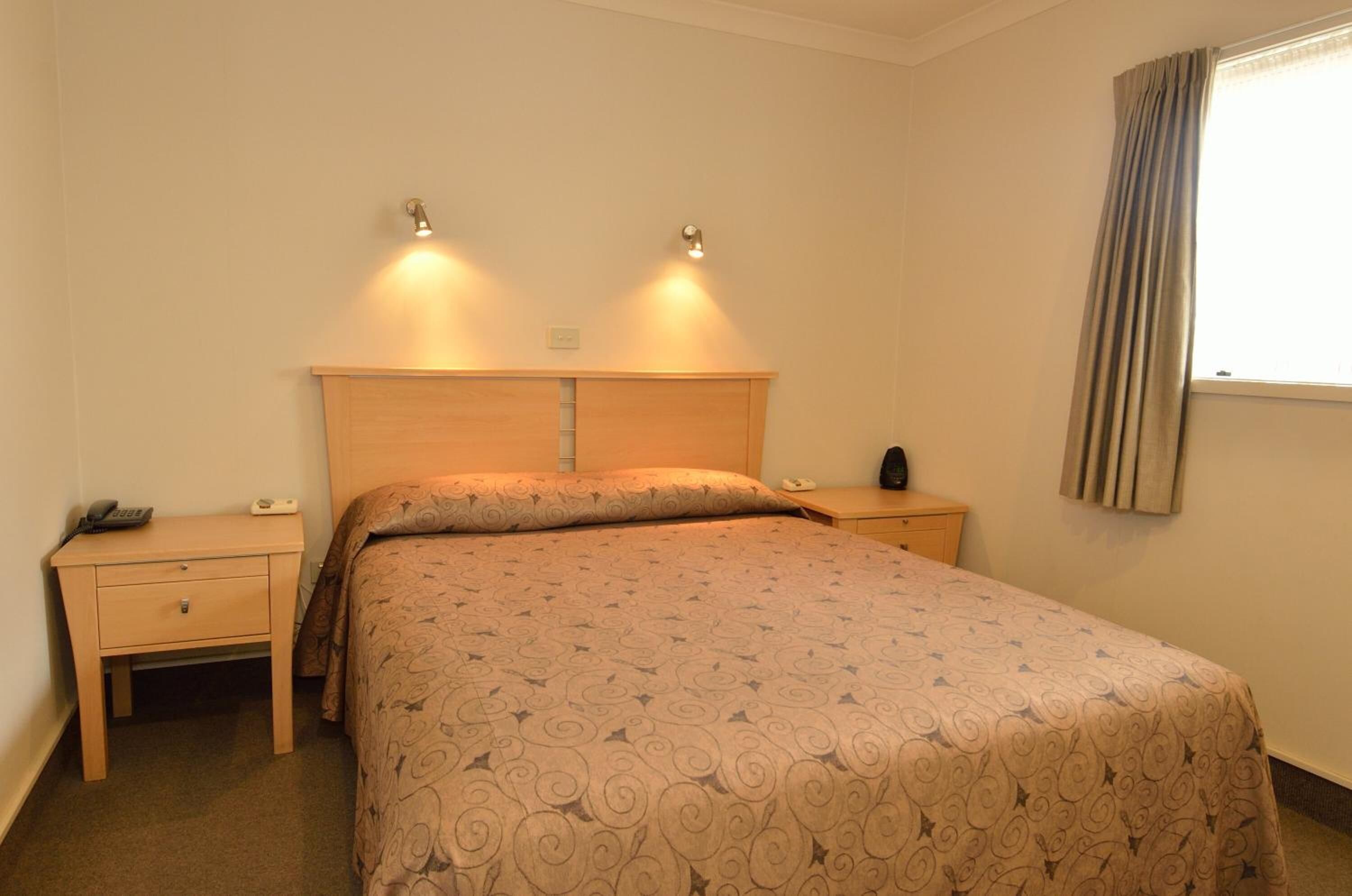 Habitación de hotel con cama, dos mesitas de noche, una lámpara y una ventana con cortinas.