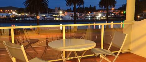 A balcony with a glass railing overlooking a marina at dusk.