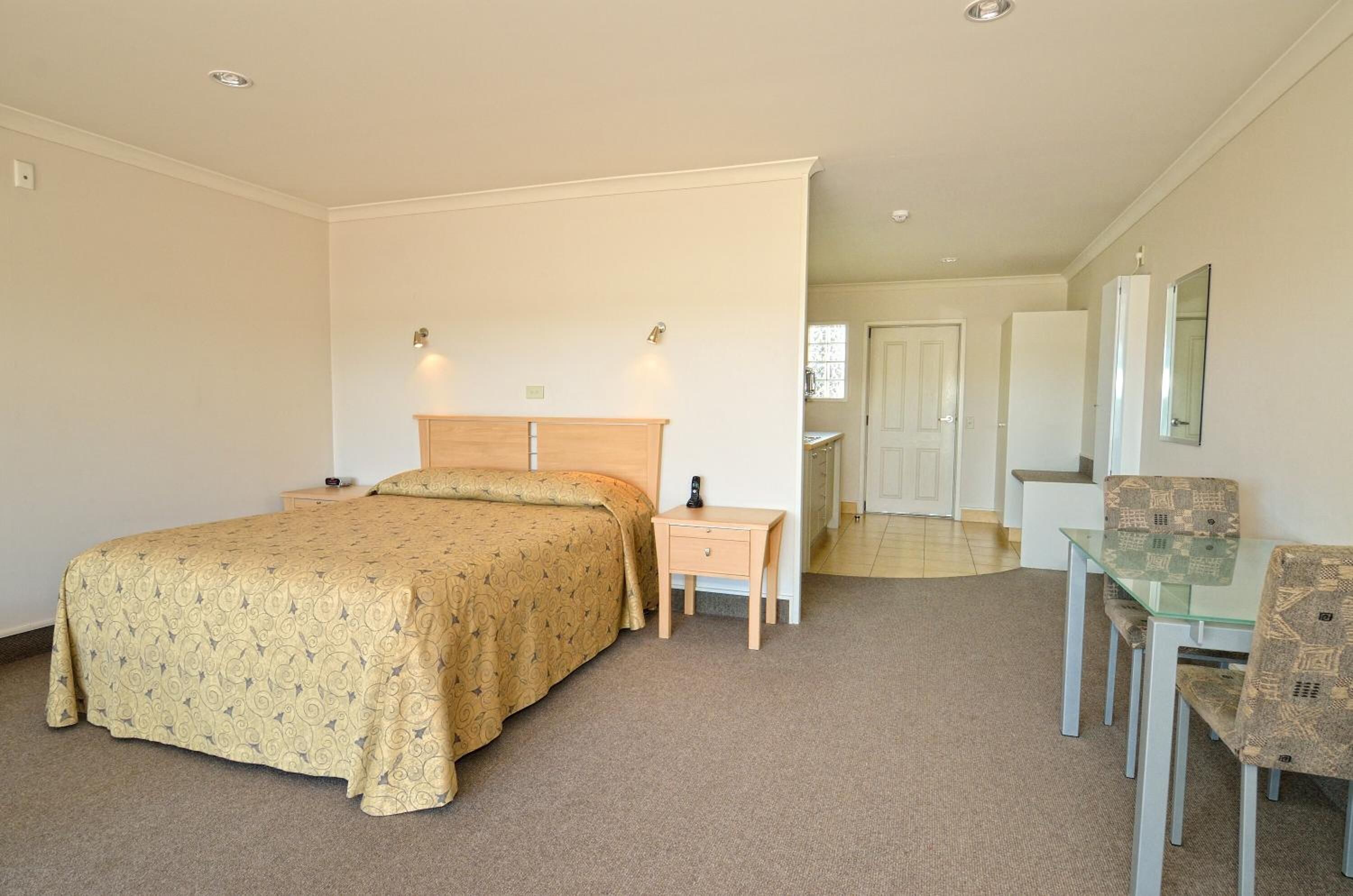 A bedroom with a bed, bedside table, and a glass table with chairs.
