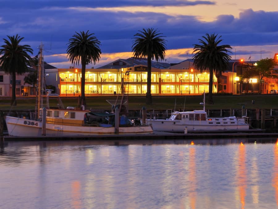 A waterfront property with boats docked, a building with multiple floors, and palm trees.