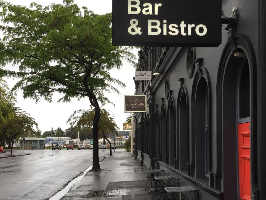 A sidewalk with outdoor seating, a sign for USSCO Bar & Bistro, and a building with arched windows.