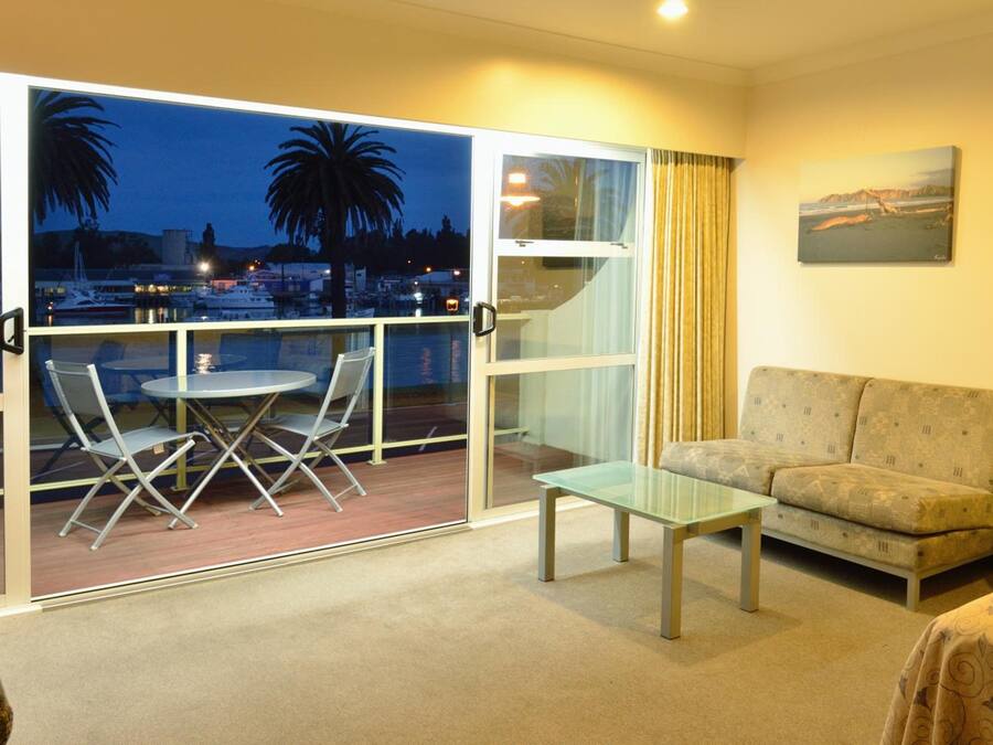 A room with a balcony, a sofa, a glass table, and a chair.