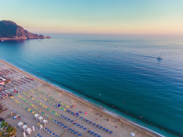 An aerial view of a beach with rows of sunbeds and umbrellas, a clear sky, and calm sea. - Lonicera City Hote (Alanya)