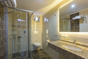 Un baño moderno con cabina de ducha de vidrio, inodoro, lavamanos con encimera de granito y un espejo grande.
