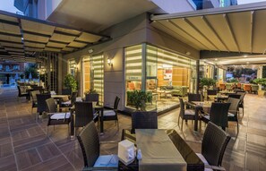 An outdoor seating area with tables and chairs, a reception desk, and a glass wall with a view of the interior. - Lonicera City Hote (Alanya)