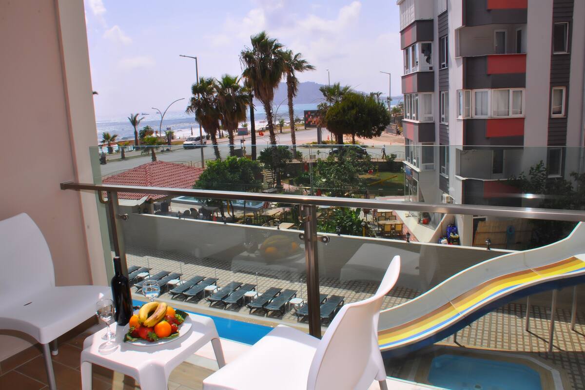 A balcony with a pool slide, lounge chairs, and a table with a bottle and fruit.