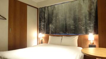 A hotel room with a bed, a round wooden table, two bedside lamps, and a large forest-themed curtain.