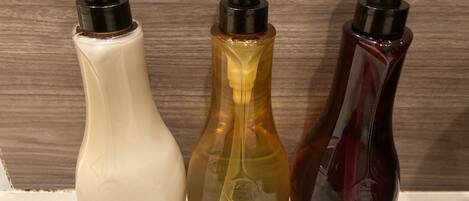 Tres botellas de productos de cuidado corporal: acondicionador, champú y jabón de baño.