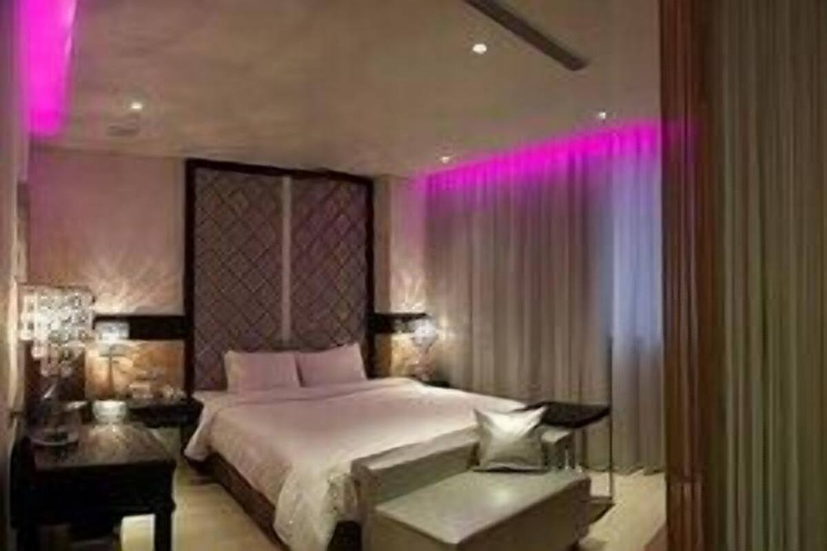 A hotel room with a bed, bedside tables, a nightstand, a window with curtains, and a bathroom with a bathtub and toilet.