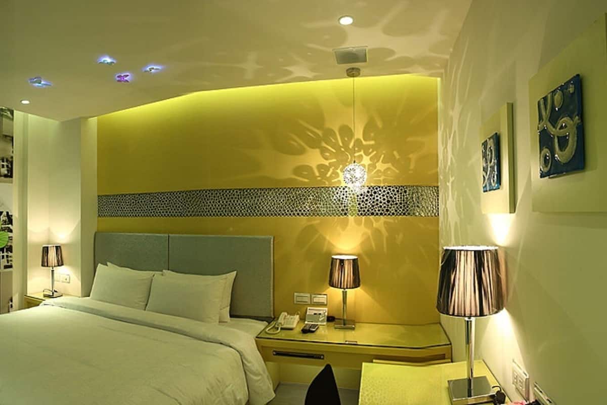 A hotel room with a bed, bedside table, lamp, and a bathroom with a sink and mirror.