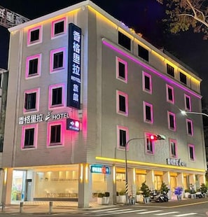 A multi-story hotel with illuminated signage, a visible entrance, and a parking area with vehicles.