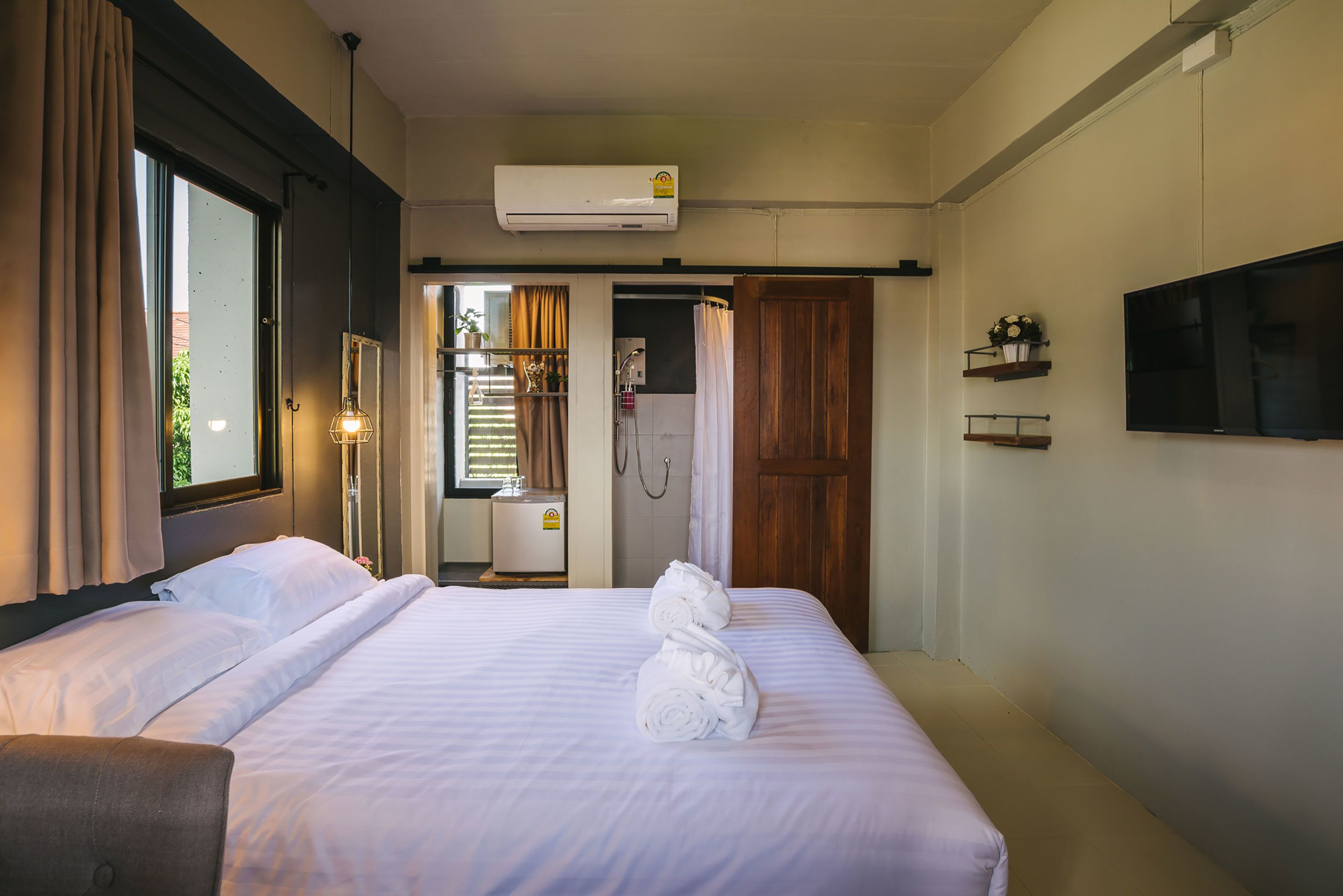 Een hotelkamer met een bed, een televisie, airconditioning, een douche en een raam met gordijnen.
