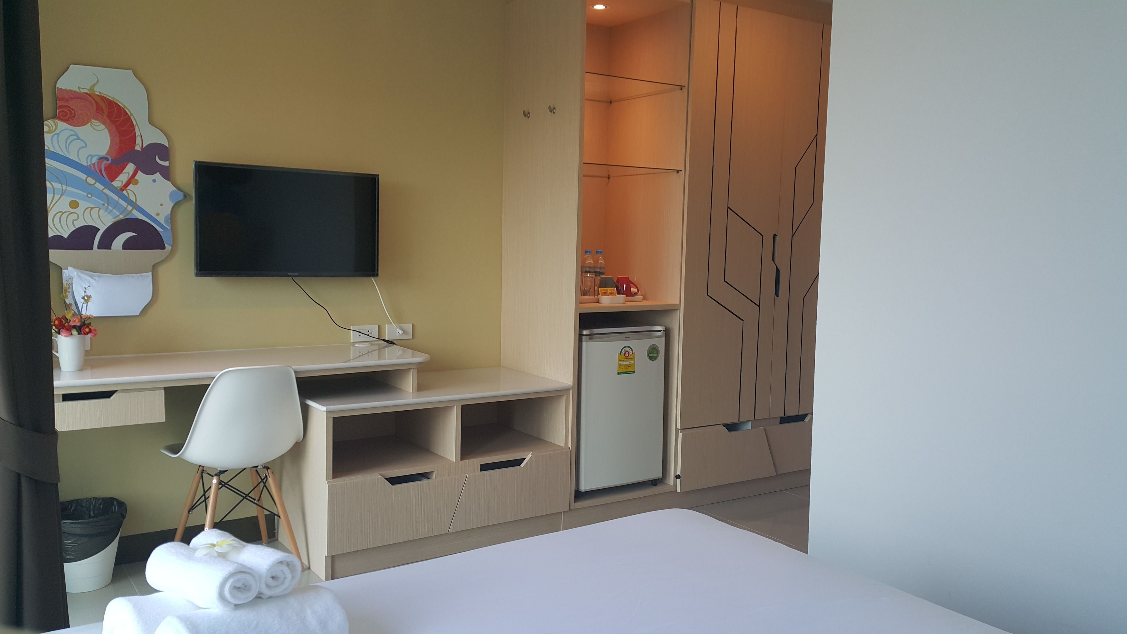 A hotel room with a bed, a desk with a chair, a television, a refrigerator, and a wall with a decorative piece.