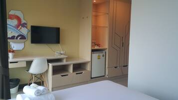 A hotel room with a bed, a desk with a chair, a television, a refrigerator, and a wall with a decorative piece.