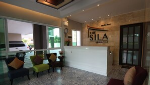 A reception area with a reception desk, several chairs, a clock, and a wall sign reading "The Sila Sriracha". - The Sila Sriracha (Si Racha)