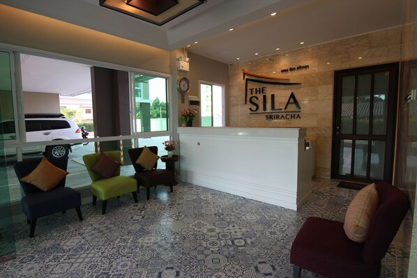 A reception area with a reception desk, several chairs, a clock, and a wall sign reading "The Sila Sriracha".
