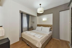 En snyggt bäddad säng med vita sängkläder, ett nattduksbord med en lampa och en modern taklampa.