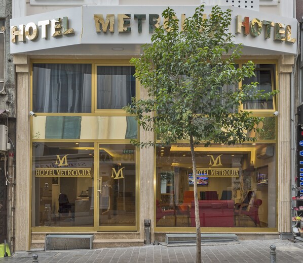 Ett hotell med en stor skylt där det står ”HOTEL METROLUX” och en väl synlig entré med ett träd framför.