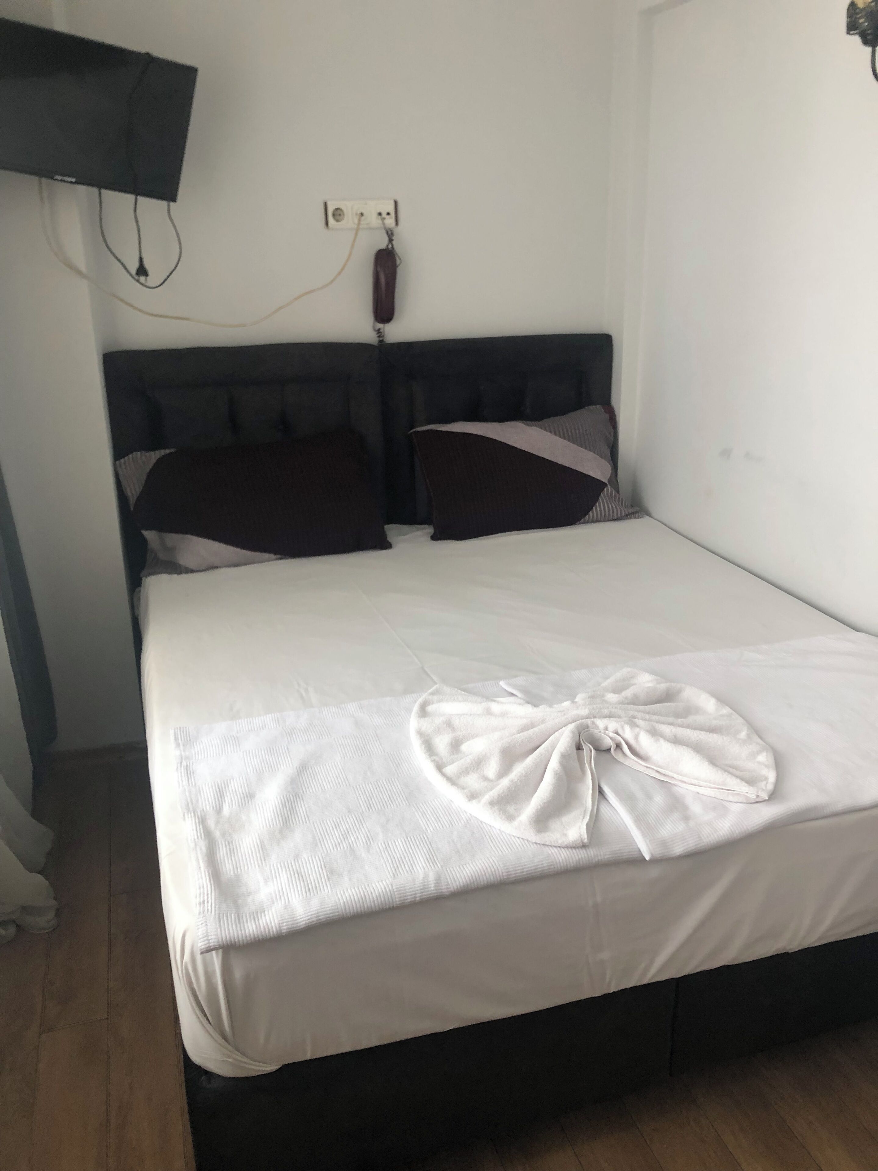 A neatly made bed with a white bedspread and a decorative bow, a dark headboard, and a wall-mounted television.