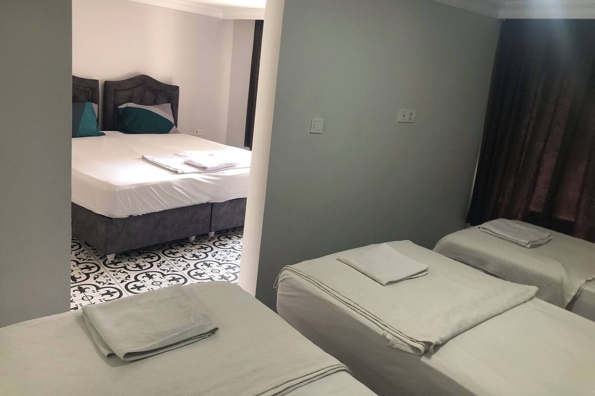 A hotel room with two single beds, a large bed, and a small table.
