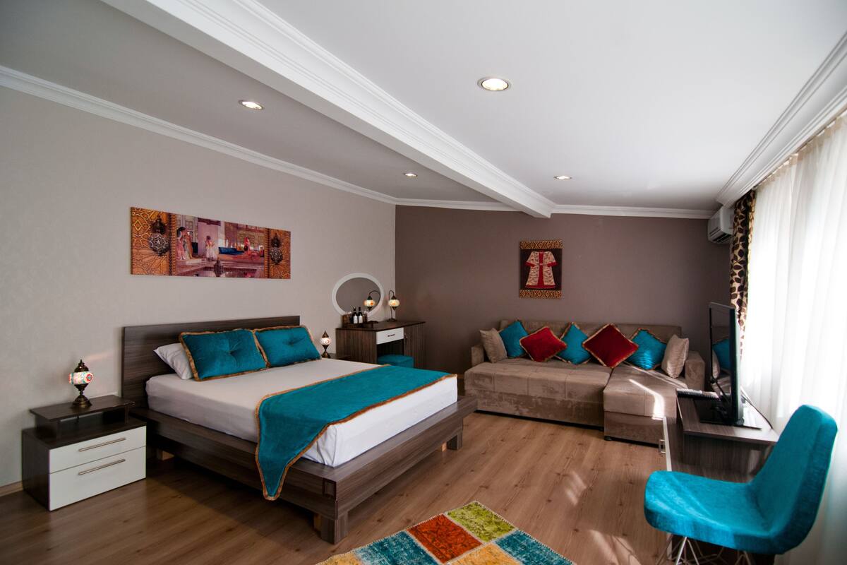 A modern bedroom with a large bed, a sofa, a desk, and a chair.