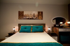 Ein ordentlich bezogenes Bett mit türkisfarbenen Kissen, ein an der Wand hängendes Bild und ein Nachttisch mit einer Lampe.