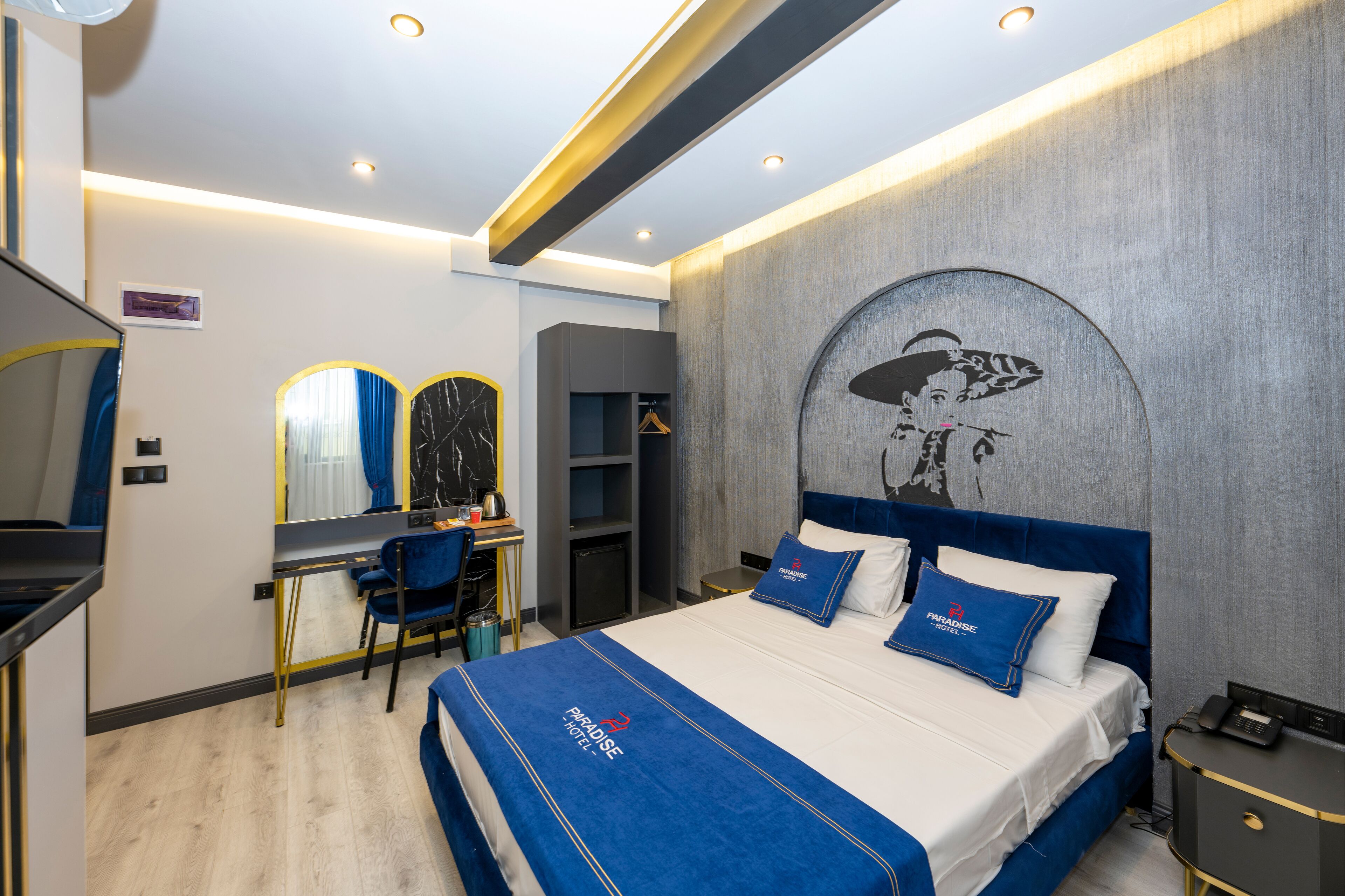 Una habitación de hotel moderna con una cama grande, un escritorio con silla, un armario y un espejo.