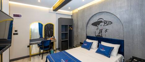 Una habitación de hotel moderna con una cama grande, un escritorio con silla, un armario y un espejo.