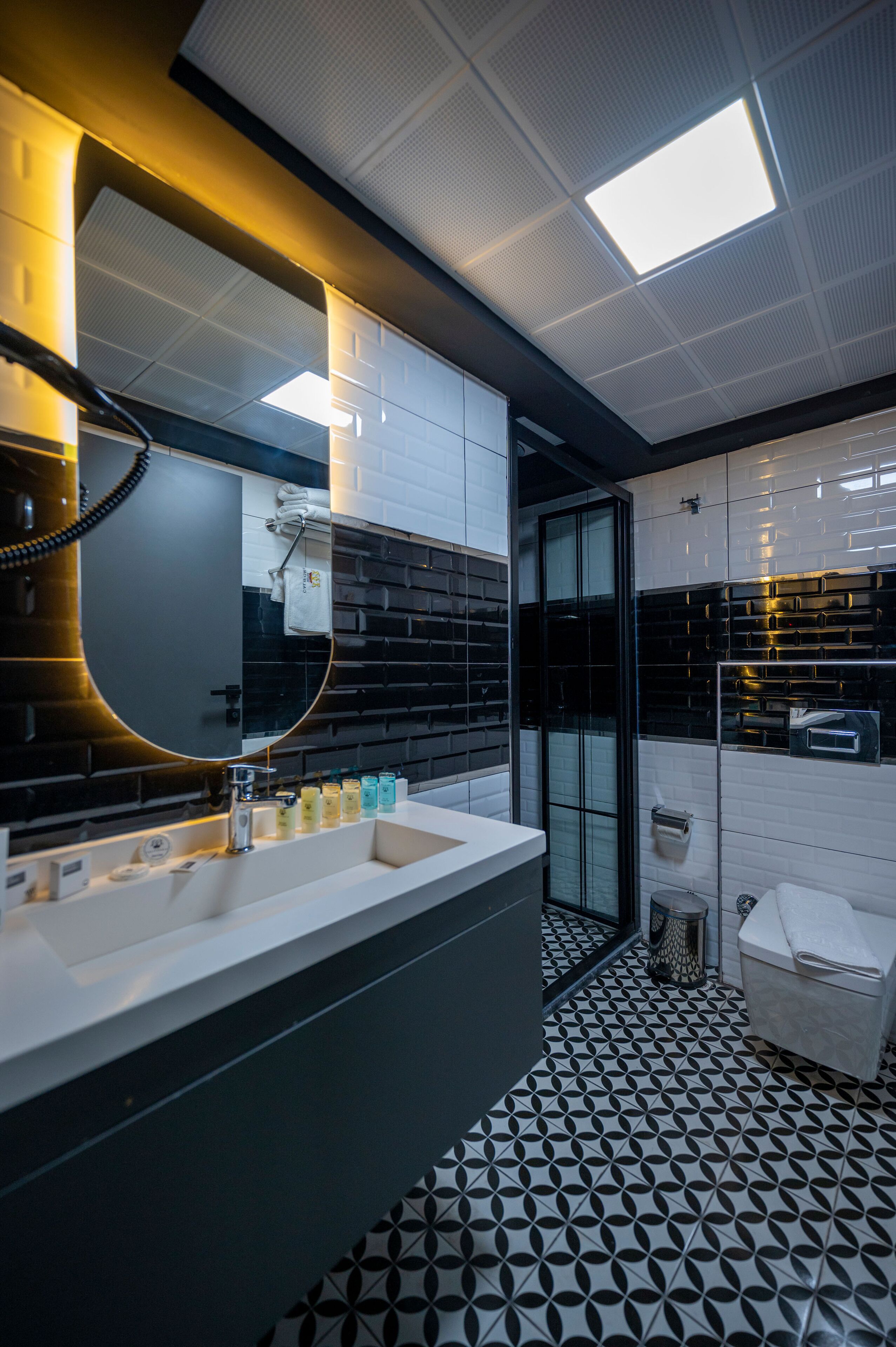A modern bathroom with a black and white tiled floor, a large mirror, and a glass-enclosed shower area.
