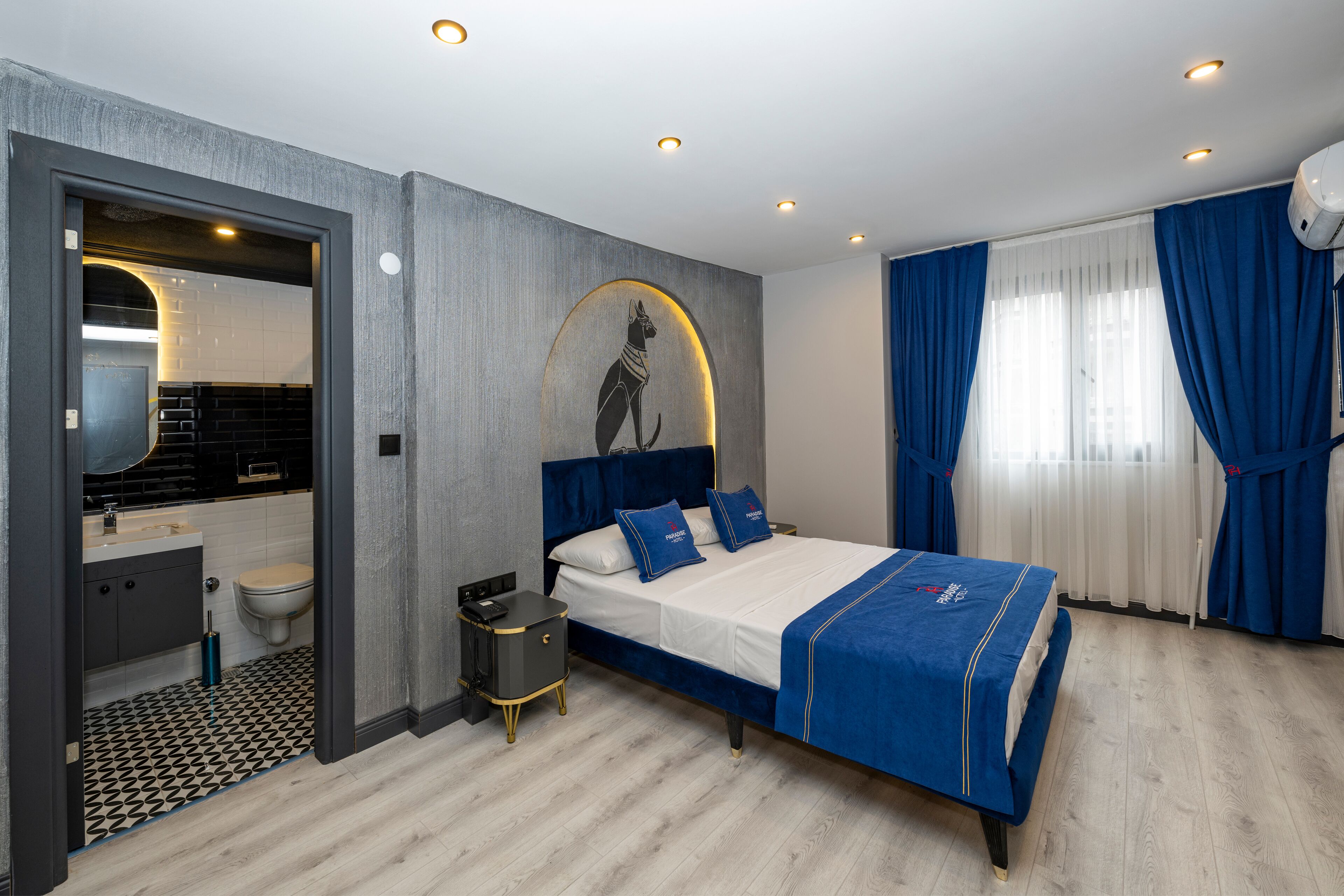 A modern bedroom with a large bed, a nightstand, a wall-mounted artwork, and a bathroom visible through an open door.