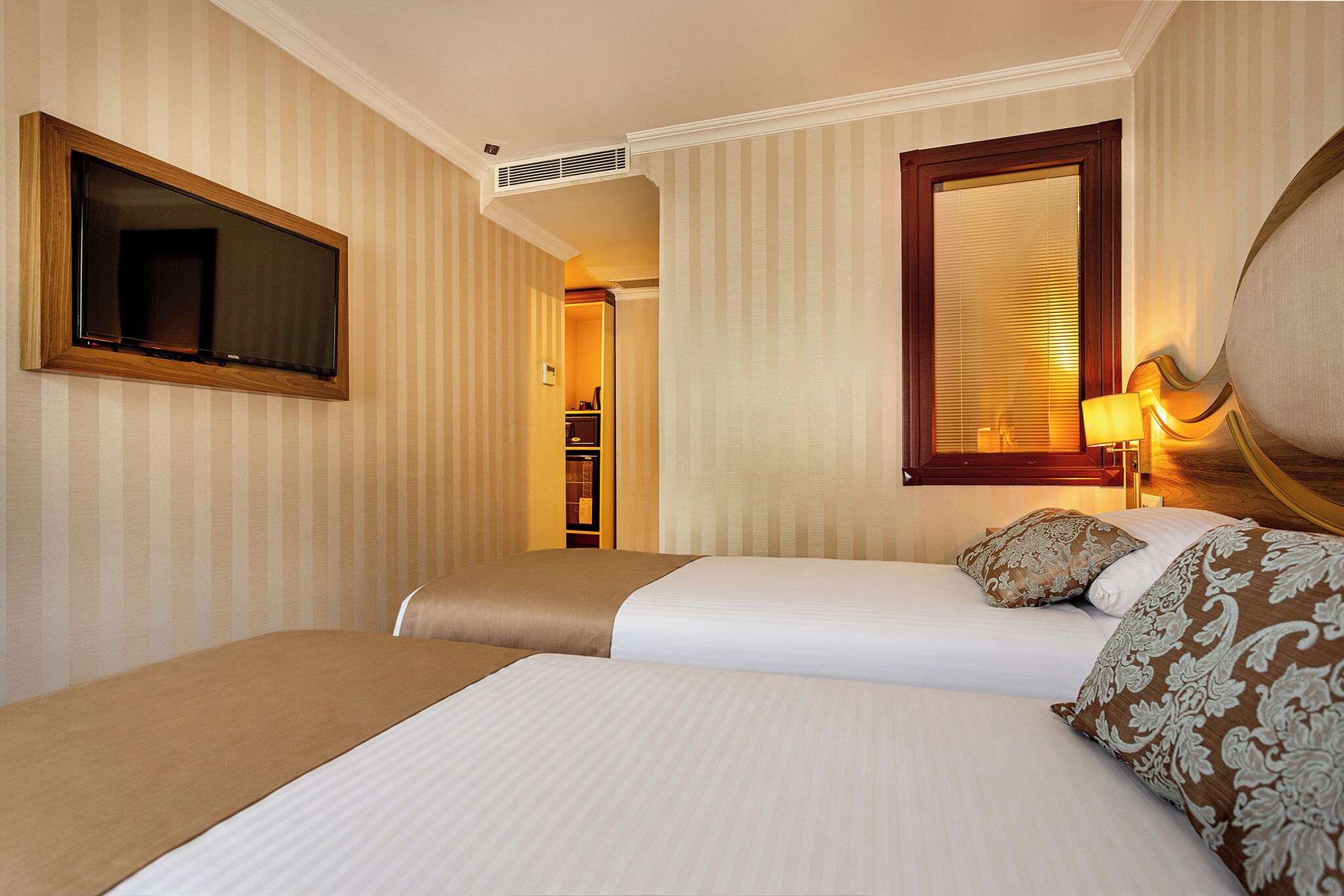A hotel room with two beds, a television, a mirror, and a bedside lamp.