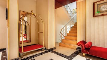 Un vestíbul d'hotel amb una catifa vermella, un ascensor daurat, una escala i un sofà vermell.