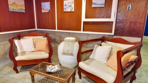 A room with two wooden armchairs, a glass coffee table, and a stack of white plates. - Maistrali (Serifos)