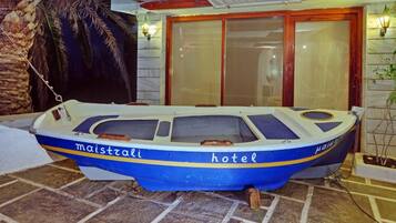 A boat with 'maistrali' and 'hotel' written on it, docked near a building with a tiled floor and a palm tree.