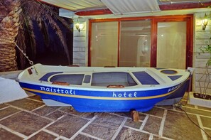 Un bateau portant les inscriptions « maistrali » et « hôtel » était amarré près d’un bâtiment dont le sol était recouvert de carreaux et qui était agrémenté d’un palmier.