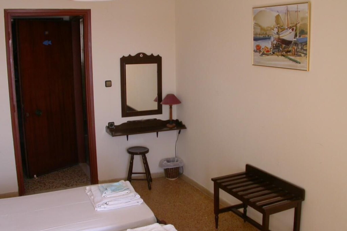 Un dormitorio con cama, un banco de madera, un escritorio con espejo y un cuadro en la pared.