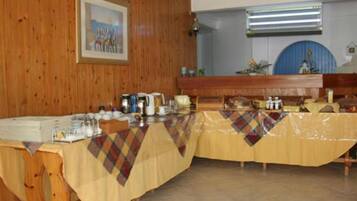 A long table with a plaid tablecloth, various dishes, and a blue wall with a framed picture.
