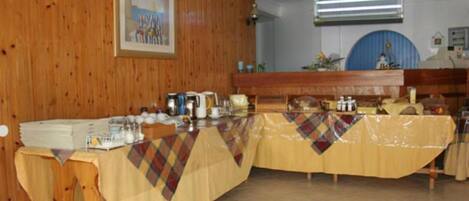 A long table with a plaid tablecloth, various dishes, and a blue wall with a framed picture.