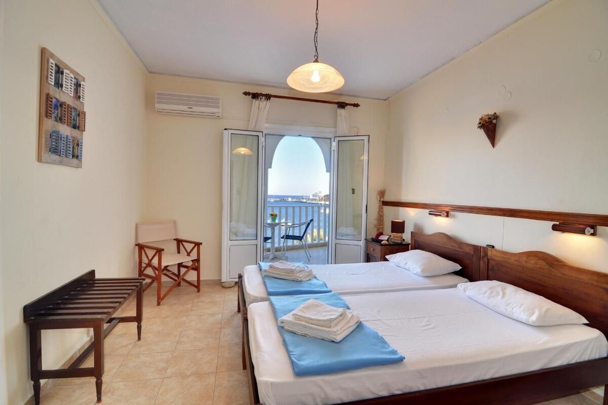 Habitación de hotel con dos camas, un escritorio, una silla y un balcón con vistas.