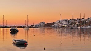 A coastal town at sunset with boats docked, white buildings, and calm water. - Maistrali (Serifos)