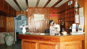 A wooden reception desk with a man talking on the phone, a vase with flowers, and a bulletin board with notices.