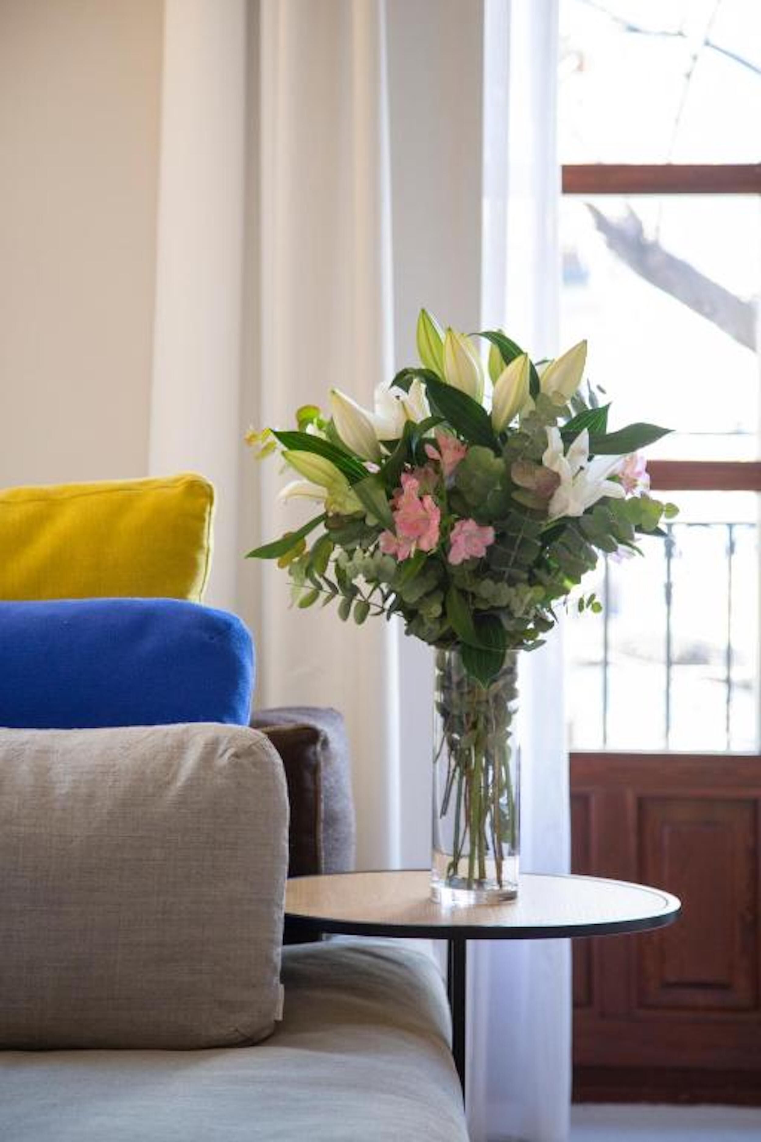 A living room with a sofa, a small round table, and a vase with flowers.