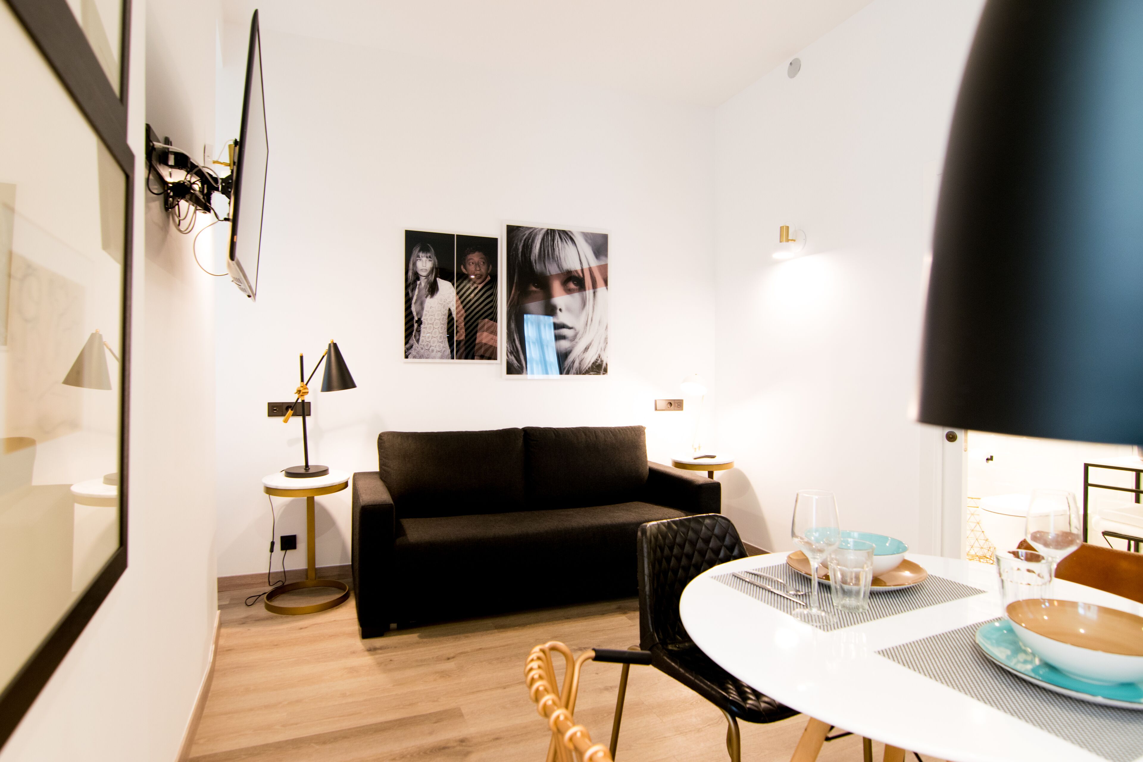 A modern living room with a black sofa, a round dining table with blue and brown plates, and a black lamp.