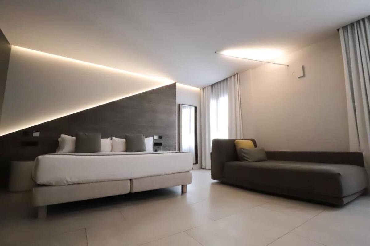 A modern hotel room with a bed, a sofa, and a large window.