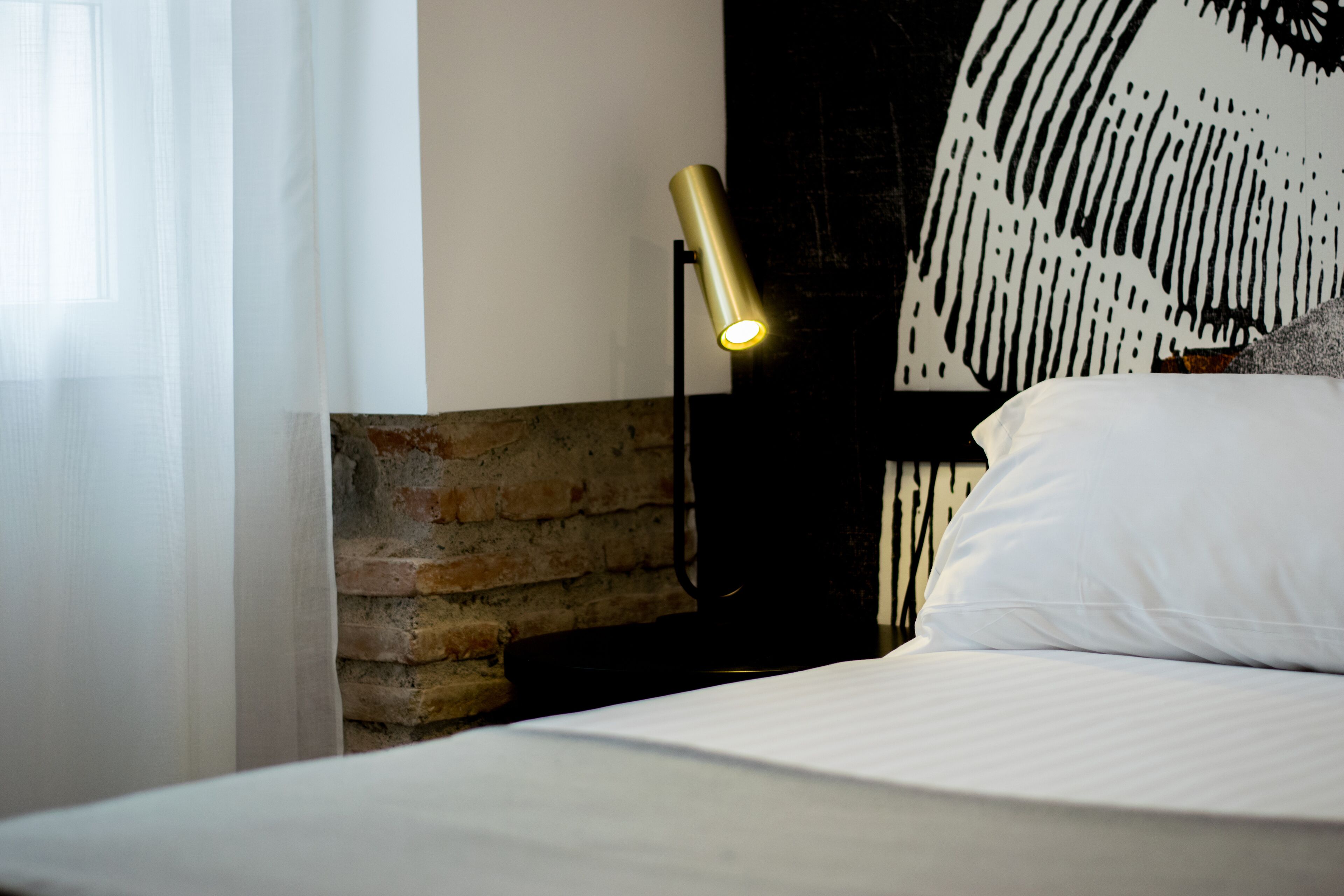Een bed met witte beddengoed, een zwart hoofdeinde en een muur met een bakstenen patroon.